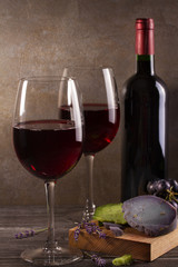 Glasses and bottle of red wine with grape, lavender and pesto cheese on chopping board. Wine and food still life