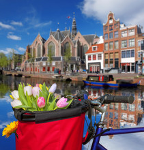 Famous Amsterdam With Basket Of Colorful Tulips Against Canal In Holland
