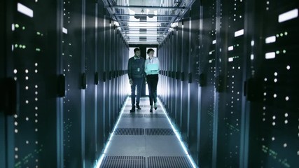 Wall Mural - Female IT Technician and Male Server Engineer Walk and Discuss Settings of a Working Data Center. Woman Holds Laptop.  Shot on RED EPIC-W 8K Helium Cinema Camera.