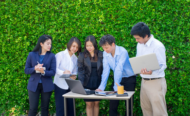 Businesswoman and businessman meeting outside office using laptop computer mobile phone and tablet device at green leaf wall,mobile office concept