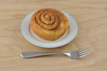 Wall Mural - Breakfast cinnamon roll on white plate with fork on wooden table