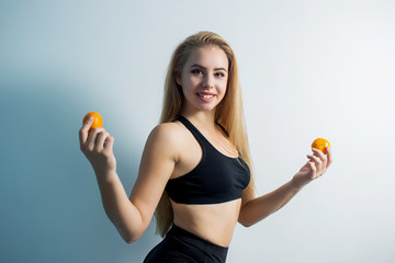 Wall Mural - girl athletic beefy beautiful body in the top of the shorts are black with long hair with raised foot holds in two hands tangerines on blue light background looking into the camera with a smile