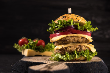 Homemade vegetarian double burger with two cutlets, tomato, cheese, green salad and purple onion on a dark wooden background