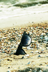 Sunglasses in black frame on sandy beach.Toned image.