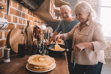 senior couple cooking pancakes on kitchen at home