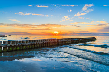 Sunset over sea with wooden breakwaters in foreground on Leba beach, Baltic Sea, Poland