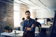 © Cavan Images - Man leaning on desk in office with colleagues in background