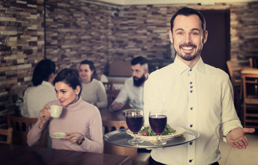 cheerful waiter taking care of adults at cafe table