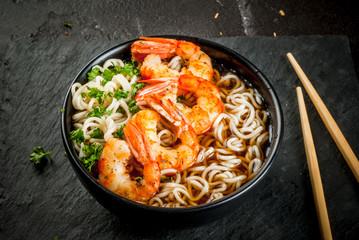 Asian soup with noodles (ramen), with miso paste, soy sauce, greens and shrimps prawn. On a black stone table, with chopsticks. Copy space