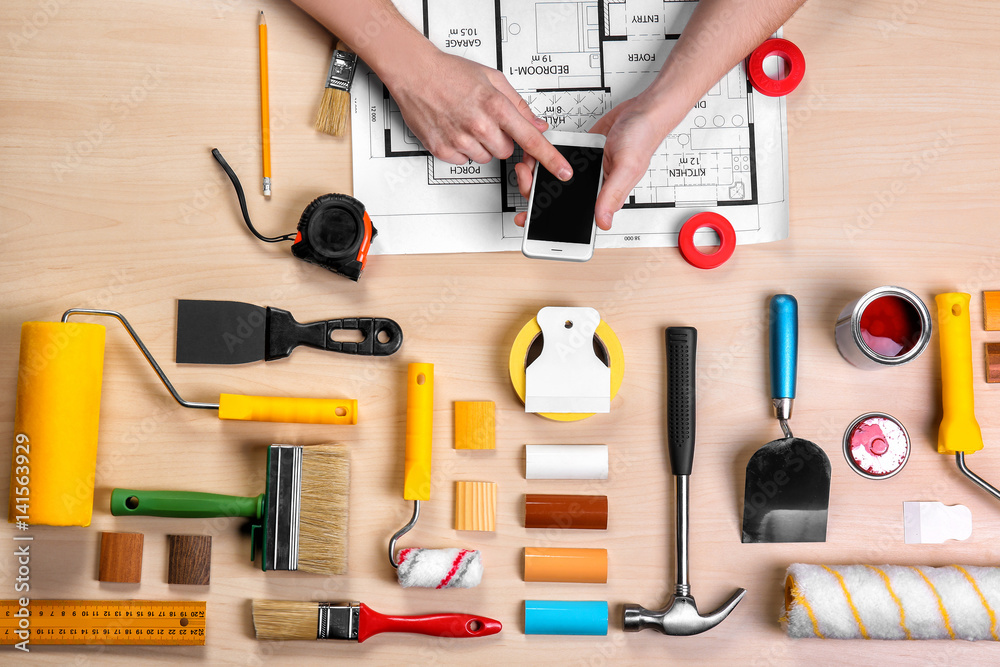 Decorator's hands with phone. Project drawing, color swatches and paint tools on work table