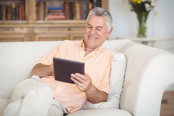 Wall Mural - Smiling senior man using digital tablet in living room