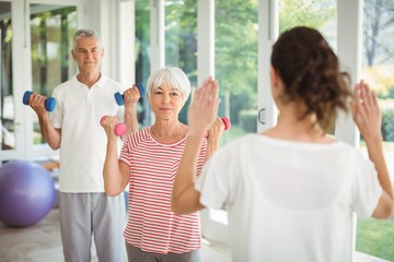 Wall Mural - Female trainer assisting senior couple in performing exercise