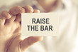 © stanciuc - Businessman holding RAISE THE BAR message card
