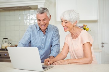 Wall Mural - Senior couple using laptop in kitchen