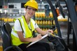 Female factory worker sitting on forklift and writing 