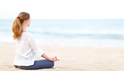 Wall Mural - woman practices yoga and meditates in lotus position on beach