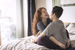 © Cavan Images - Cheerful lesbians sitting face to face on bed at home