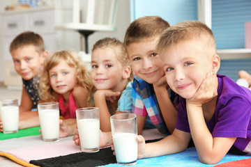 Poster - Cheerful children with glasses of milk lying on colourful carpet in the room