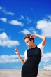 © raisondtre - Wonderful portrait of a young slim woman in a black dress with a white bolero posing on a background of blue sky and white clouds of air