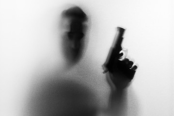 Shadow of horror man killer with a gun in his hand.Dangerous man behind the frosted glass.Mystery man.Halloween background.Black and white picture.Blur picture.