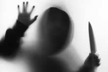 Shadow Blur Of Horror Man In Jacket With Hood Knife In His Hand.Dangerous Man Behind The Frosted Glass.Mystery Man.Halloween Background.Black And White Picture.Blur Picture.