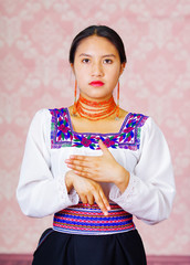 Wall Mural - Young woman wearing traditional andean dress, facing camera doing sign language word for son