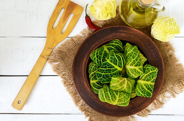 Wall Mural - Leaves of Savoy cabbage stuffed with minced meat and rice in a clay bowl on a light background. Top view.