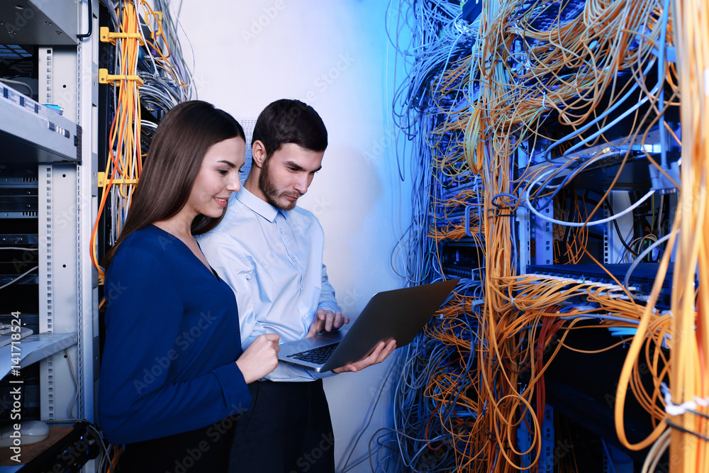 Young engineers with laptop in server room