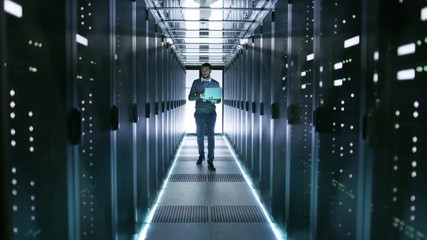 Wall Mural - Male Server Engineer Walks with Laptop Through Working Data Center Full of Rack Servers. Shot on RED EPIC-W 8K Helium Cinema Camera.