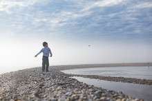Boy Standing On Pebbled Beach Throwing Pebbles