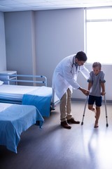 Canvas Print - Doctor assisting injured boy to walk with crutches