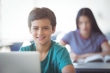 portrait of happy schoolboy using laptop in classroom