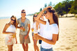 © maxbelchenko - Beautiful girl with glasses is holding a bottle with beer in her hands. Group of friends hanging out with beer at the beach.  Excellent sunny weather. Beautiful figures. Super mood. Summer concept