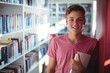 Portrait of happy schoolboy holding book in library