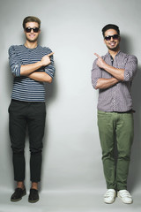 Look at this! Two good looking young men in casual clothes smiling and looking at camera while standing against grey background