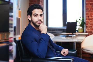 Wall Mural - The portrait of Arab businessman in suit jacket sitting in a leather chair in office