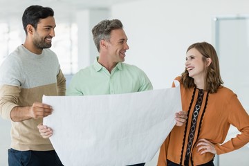 Wall Mural - Smiling business colleagues discussing over blueprint