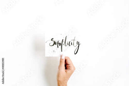 Plakat Minimal pale composition with girl's hand holding card with word Simplicity written in calligraphic style on paper on white background
