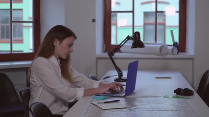 Aufkleber - Young caucasian architect working in creative office. Professional designer sitting the the table with blueprint. Lady wearing in casual dress typing on computer.