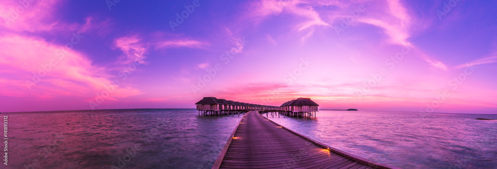 Sunset on Maldives island, water villas resort. Beautiful sky and clouds. Beautiful beach background for summer travel with sun, beach wooden jetty. Summer mood sun beach background concept. - obrazy, fototapety, plakaty 