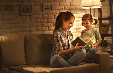 Family before going to bed mother reads to her child daughter book near a lamp in the evening