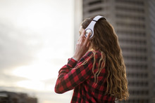 Side View Of Woman Wearing Headphones While Standing Against Building