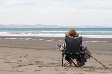 Old lady sits on empy ocean shore