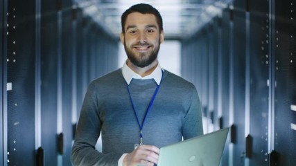 Wall Mural - Male Server Engineer Works on a Laptop in Data Center then Smiles. Shot on RED EPIC-W 8K Helium Cinema Camera.
