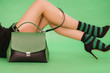 Young fashion styled woman is lying in colored socks with green and black handbag on a green background, concept style