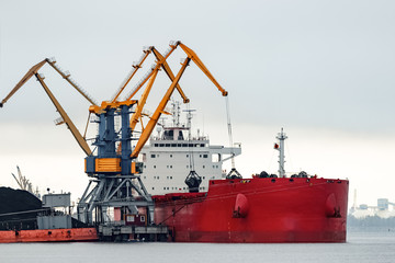 Large red cargo ship loading with a coal in the port