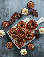 Wall Mural - donut rings and vanilla caramel cupcakes with white and dark chocolate chippings and icing served on board