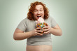 © WHstudio Leushin N - Excited happy obese young man with ginger curly hair opening mouth widely while eating candy floss out of glass jar full of colorful sweets. Obesity, gluttony and unhealthy lifestyle concept