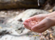 Closeup Of Tap Water Droped Into Woman Hands, Natural Sandy Background. Protect Water Resource For Our Planet.