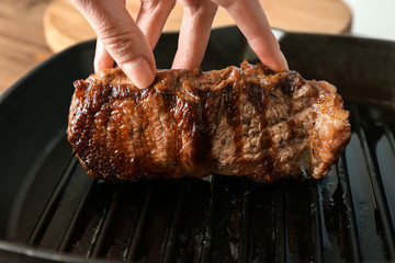 Wall Mural - Hand holding juicy steak on grill pan